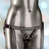 A shiny, silver-colored mannequin is adorned with the luxurious *Her Royal Harness The Regal Duchess Pewter* by CalExotics, featuring ornate and intricate detailing with metallic accents. Crafted from vegan leather, the harness belt includes an adjustable buckle. The background features a soft, out-of-focus, colorful bokeh light pattern.